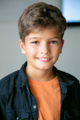 Portrait of Caucasian little boy with stylish haircut. Cute happy child posing in classroom after lesson, smiling and looking at camera. Front view. People, study and appearance concept