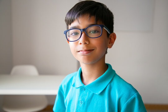 Portrait Of Asian Little Boy In Eyeglasses. Cute Confident Child Posing In Classroom After Lesson, Smiling And Looking At Camera. Front View. People, Study And Appearance Concept