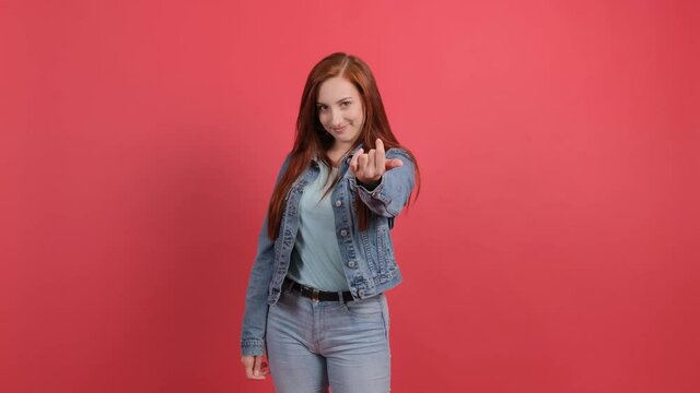 Come to me. Young woman pointing at someone to come, isolated on red background.