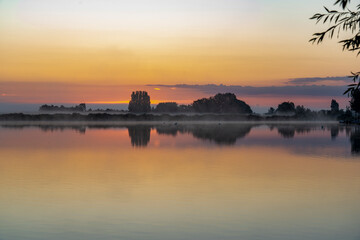 Just before sunrise, the morning mist above lake Noordhovense plas and the clouds above the horizon, create a colorful spectacle