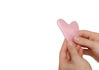 Neat female hands of a cosmetologist masseur hold a gouache scraper made of pink jade in the shape of a heart. Face body skin care concept, anti-aging facial treatment. Isolated, copy space