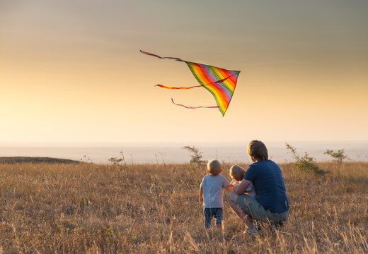 Dad And Kids Boys Fly A Kite At Sunset.