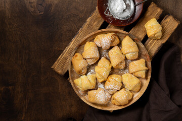 Lots of bagels. Puff pastry in a wooden plate on a brown table. Cookies close-up. Top view with space for text