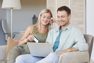 Young couple sitting together on sofa using laptop to pay online with credit card