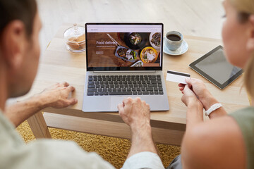 Image of laptop with food delivery site on the screen with young couple paying for order