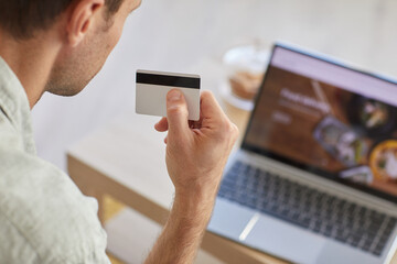 Rear view of man holding credit card and paying for food delivery online using laptop