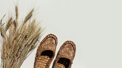 Pair of old bast shoes and a sheaf of wheat on a light background.