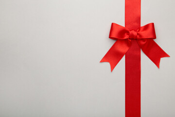 Red ribbon with bow with tails on grey background.