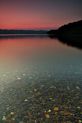夕暮れの湖。湖面に映る黄昏の空と山並みのシルエットから成る静寂の印象。