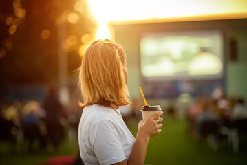 Open-air cinema. Girl with a glass of coffee watching a movie in a summer cinema.