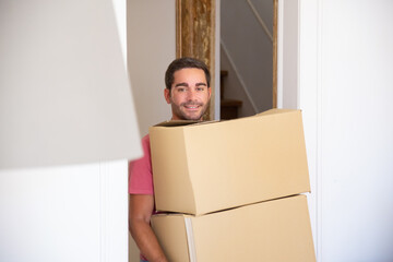 Happy man moving into new apartment, walking through doorway and carrying boxes. Side view. Loader occupation or delivery service concept