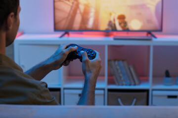 Rear view of young man holding joystick and watching TV he playing in video game