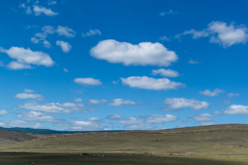white bright fluffy light clouds in blue sky with green grass hills, open space