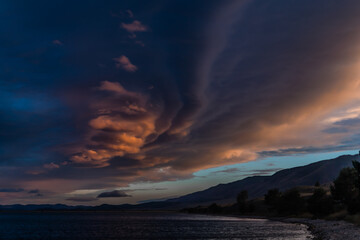 colorful bright red orange pink sunset with blue clouds on pebble coast of the bay of lake with trees