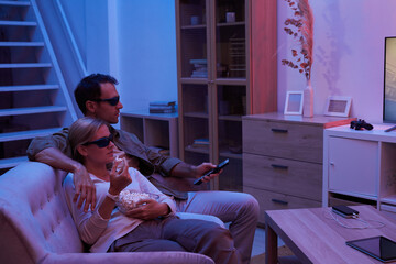 Young couple sitting on sofa in 3D glasses and watching TV in dark living room