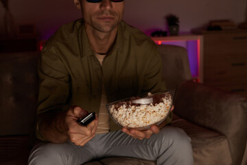 Fototapeta na wymiar Close-up of young man holding bowl with popcorn and remote control and watching TV on sofa at home