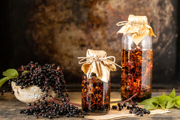 Fresh black elderberry syrup in a glass bottle on a wooden table. Copy space