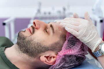 Fototapeta na wymiar Attractive man receiving botox injection in the forehead area. Doctor makes cosmetic injection. Beauty treatment.