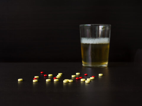 Ecstasy Pills with blur image of beer in glass on black background. Popular drink with beer. Dangerous drug. Addictive substance. narcotic concept.