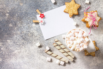 Christmas background. White list and cup of hot cocoa with marshmallows and Christmas baking on a stone countertop.  Top view flat lay background. Copy space.