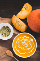 Pumpkin soup in a bowl with seeds and fresh pumpkin on wooden background