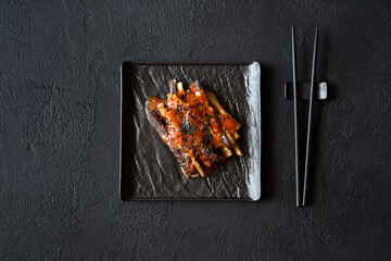 Eggplant slices in a spicy red sauce decorated black sesame seeds on dark concrete background. Top view. Asian food