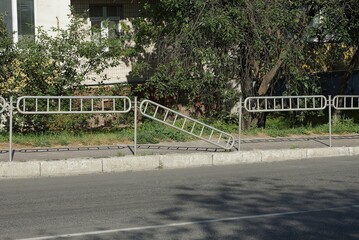 gray metal fence with a broken section on the street near the curb and asphalt road against the background of green vegetation
