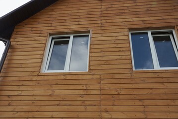 two white windows on a brown wall of a house made of wooden boards