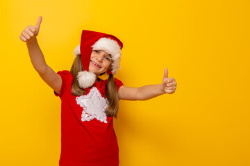 Fototapeta na wymiar Little girl wearing Santa hat holding thumbs up