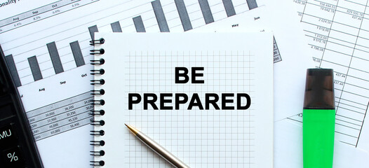 Text BE PREPARED on the page of a notepad lying on financial charts on the office desk. Business concept.