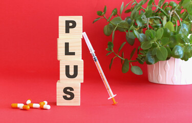 The word PLUS is made of wooden cubes on a red background with medical drugs. Medical concept.