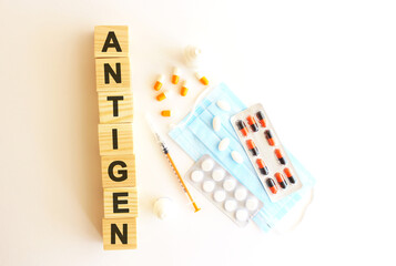 The word ANTIGEN is made of wooden cubes on a white background with medical drugs and medical mask. Medical concept.