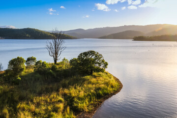 Island overgrown with grass and trees on lake and misty mountains view