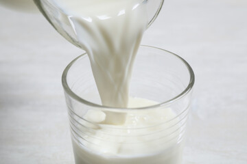 Pouring milk into glass on white table, closeup