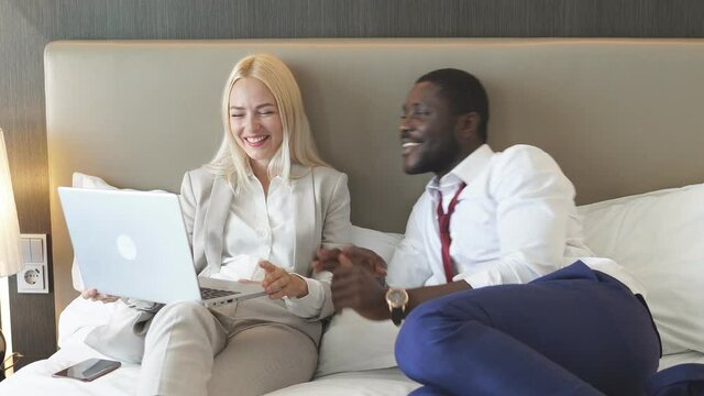 Happy family spends time on a business trip, watching news on laptop lying on bed in hotel.