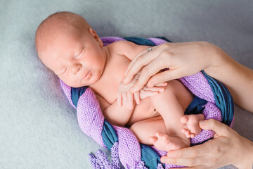 Adorable newborn baby wrapped in a beautiful fabric, woolen scarf and with a small hat on his head