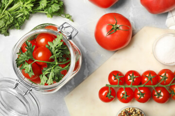 Pickling jar with fresh ripe cherry tomatoes and spices on grey table, flat lay