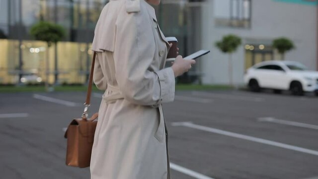 Cropped shot of unrecognizable woman in trench coat walks with smartphone in the city