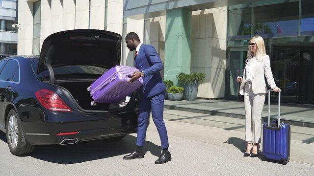 black man puts luggage in a car, confident african bellboy serve clients of hotel