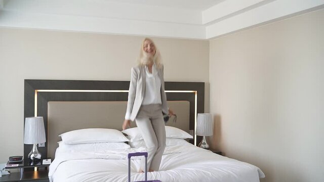 Cheerful woman dance on bed in hotel, have rest after hard working days, enjoy.