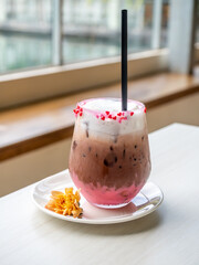 Iced dark chocolate with mild foam, decorated with sweet sugar small heart in glass on table, under natural light