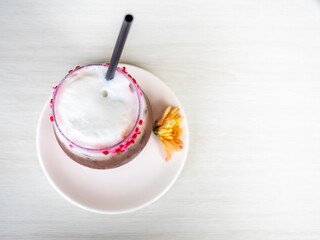 Iced dark chocolate with mild foam, decorated with sweet sugar small heart in glass on table, under natural light