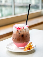 Iced dark chocolate with mild foam, decorated with sweet sugar small heart in glass on table, under natural light