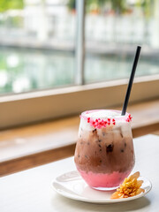 Iced dark chocolate with mild foam, decorated with sweet sugar small heart in glass on table, under natural light