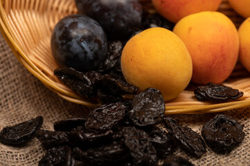Ripe apricots, juicy black plums and dried prunes in a wicker basket. Close up. Autumn harvest.