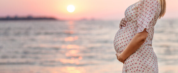unrecognazible pregnant woman on the coast sunset. The concept of expectation of a child calm pacification silence. Gentle tones of tenderness. Place for text. belly close-up.