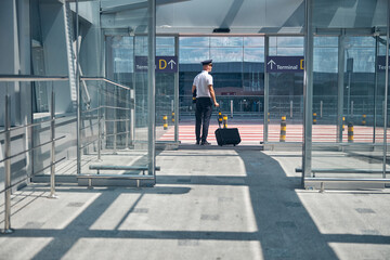 Male pilot with travel suitcase standing outside airport terminal