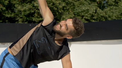 Adult handsome bearded man doing fitness on rooftop. Outdoors meditation and wellness lifestyle concept on summer sunny day. Portrait of attractive caucasian young man doing yoga exercises