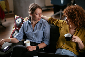Girlfriends talking and laughing in office. Beautiful women drinking coffee in the office