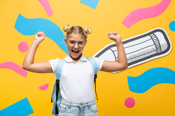 excited schoolgirl in eyeglasses showing winner gesture near paper pencil and multicolored elements...